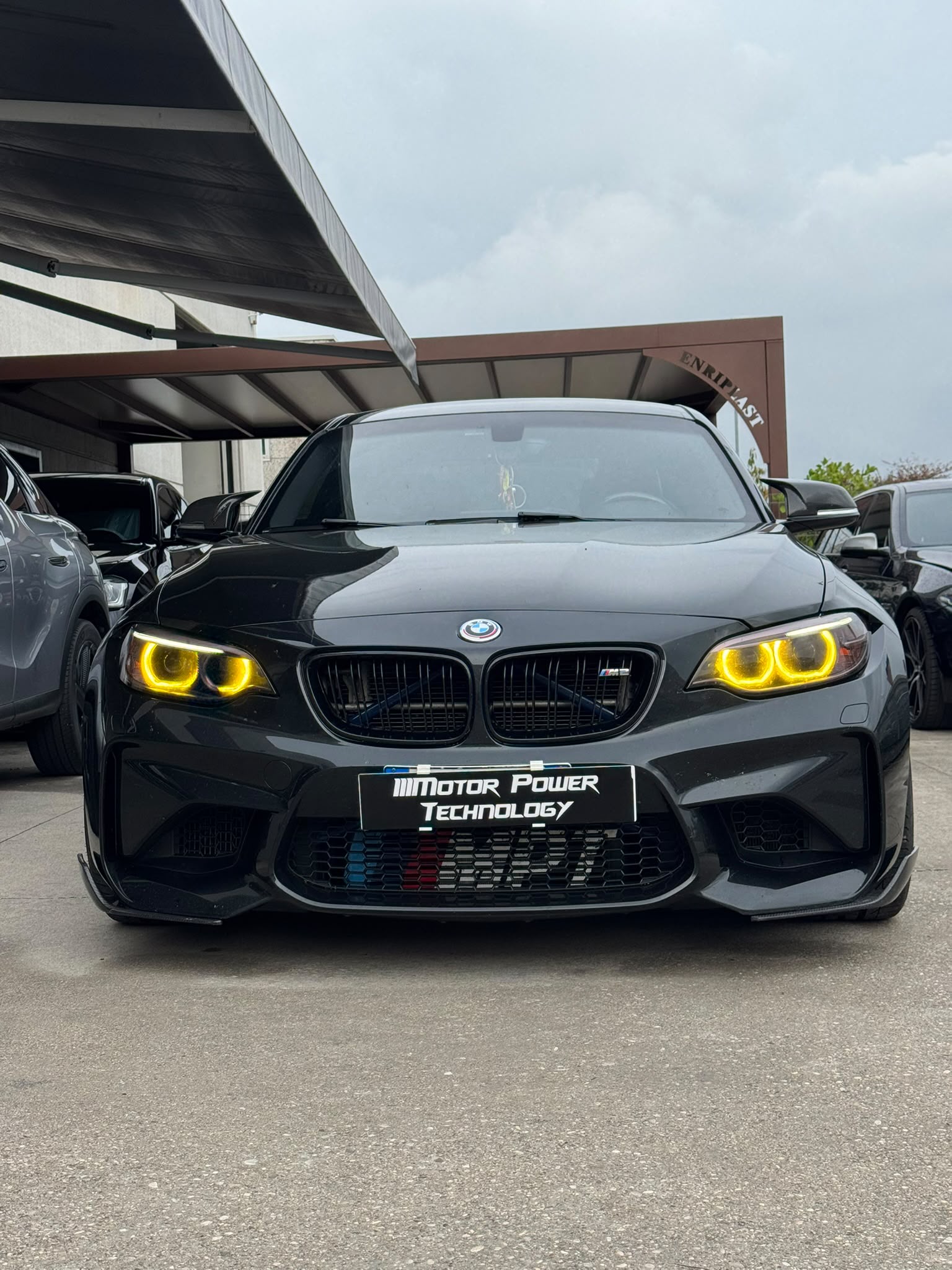 Preparazioni auto – BMW M2 nera con fari gialli nel piazzale